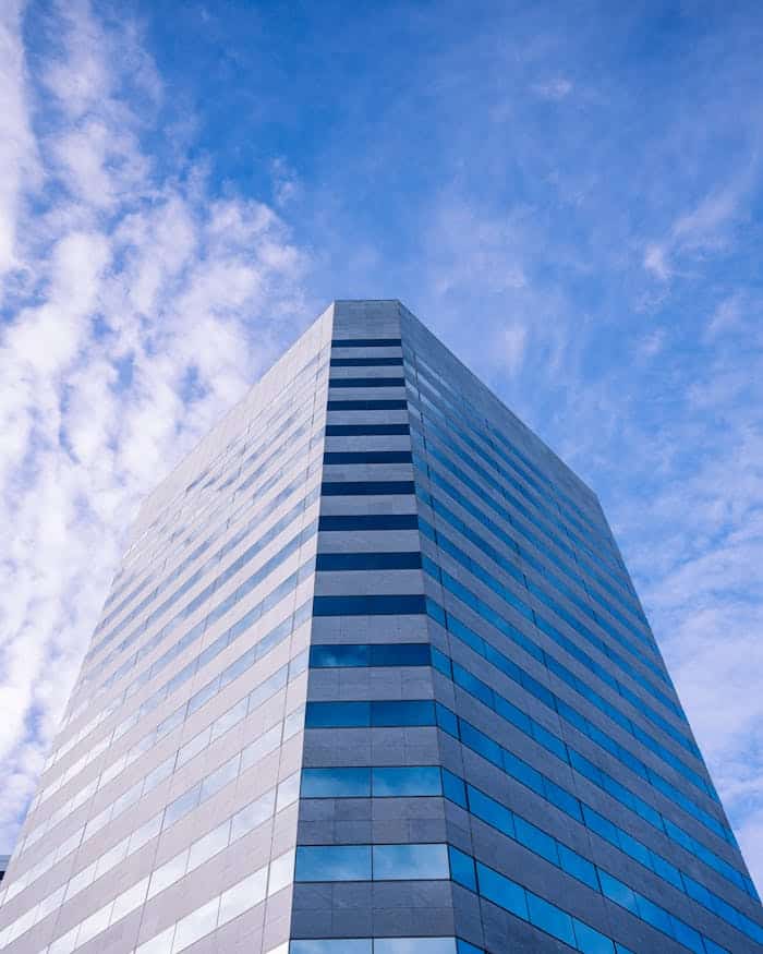 about-us-02 From below exterior of contemporary multistory office building located on sunny street against blue sky with clouds in city center